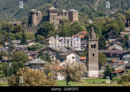 Il campanile della chiesa parrocchiale di San Maurizio, con sullo sfondo l'imponente castello di Fénis, Valle d'Aosta, Italia Foto Stock