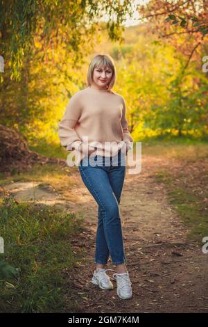 Una donna bionda con un taglio corto cammina attraverso la foresta in un maglione a maglia. Escursioni all'aperto nella foresta autunnale. Foto Stock