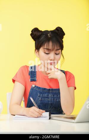 Pensivo giovane donna graziosa che scrive nel copybook quando fa i compiti di matematica e risolvendo le equazioni Foto Stock