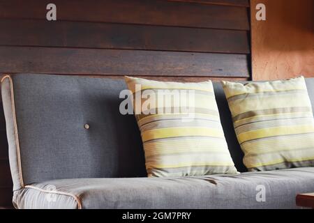 Divano grigio con due cuscini posto accanto alla parete di legno marrone. Luce naturale del giorno. Foto Stock