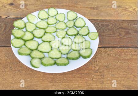 Cetrioli freschi tagliati in un piatto su sfondo di legno - benefici del concetto di cetrioli Foto Stock