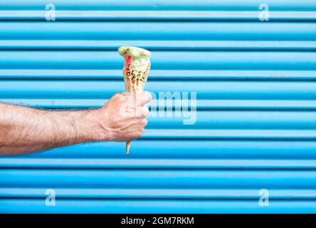 mano dell'uomo che tiene un cono del gelato che si fonde su uno sfondo blu chiaro Foto Stock