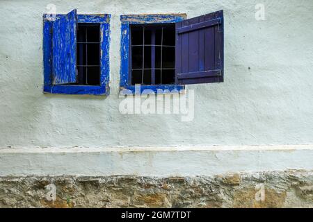 Vecchie finestre di legno blu in un muro imbiancato con macerie sulla base di pietra Foto Stock