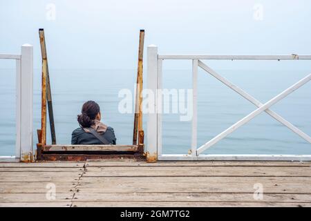 Donna che gode la calma placida su un molo con scale e pavimenti in legno sulla riva del Mar Nero Foto Stock