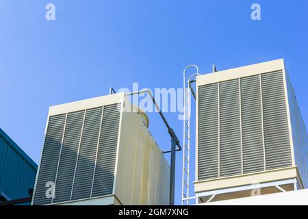 Torri di raffreddamento industriali o refrigeratori raffreddati ad aria sul tetto della nuova fabbrica di edifici con sfondo blu cielo Foto Stock