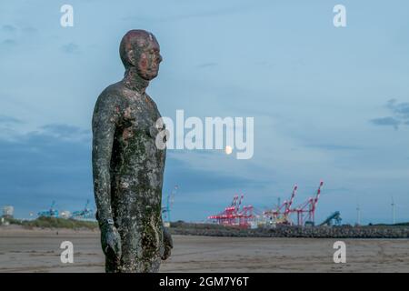 La luna sorge su un Iron Man e Seaforth Docks sulla spiaggia di Crosby vicino a Liverpool nel settembre 2021. Foto Stock