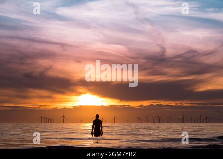 Uno degli Iron Men di Antony Gormley sulla spiaggia di Crosby vicino a Liverpool visto nel settembre 2021 guardando il tramonto sopra il parco a vento di Burbobank nella se irlandese Foto Stock