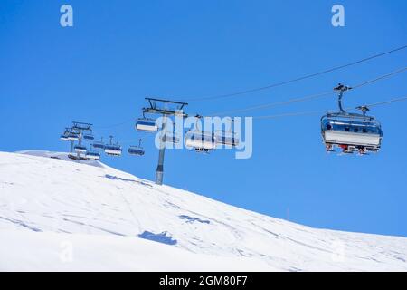 La gente si alza sugli impianti di risalita con posti a sedere che si snodano sulla montagna e sentieri da cieli e snowboard Foto Stock