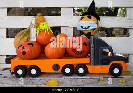 Grande giocattolo per bambini arancione auto camion caricato con molte zucche. Uno di loro indossa una maschera medica, una bottiglia di igienizzante è nelle vicinanze. Halloween cel Foto Stock