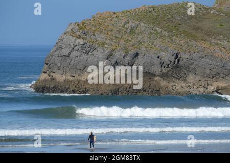 Il surfista si prepara a pagaiare nel surf perfetto a questa spiaggia sul Gower al riparo dal vento dalla ripida isola di Burry Holmes Foto Stock