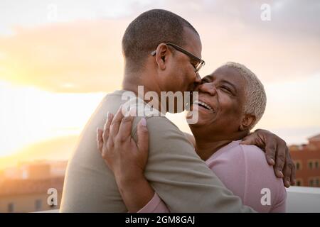 Felice coppia latina anziana che ha un momento romantico abbracciando sul tetto Durante il tramonto - gli anziani amano il concetto Foto Stock