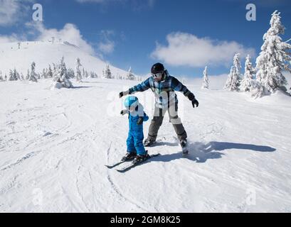 Bambino ragazzo felice bambino imparando a sciare con suo padre durante le vacanze invernali in montagne innevate in giornata fredda di sole Foto Stock