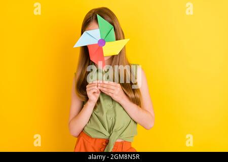 Foto ritratto schoolgirl indossare camicia verde sorridente volto nascosto con mulino isolato colore giallo vivo sfondo Foto Stock