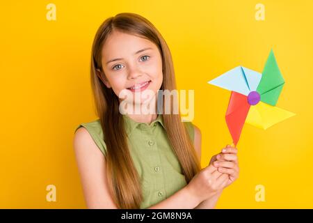 Foto ritratto schoolgirl indossare camicia verde sorridente giocando con mulino isolato colore giallo vivo sfondo Foto Stock