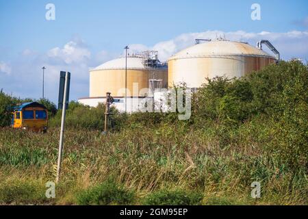 GB Railnight Class 66 attende di attraversare A228 a Grain Crossing sull'isola di Grain con serbatoi National Grid Liquid Natural gas Storage dietro Foto Stock