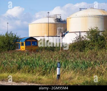 GB Railnight Class 66 attende di attraversare A228 a Grain Crossing sull'isola di Grain con serbatoi National Grid Liquid Natural gas Storage dietro Foto Stock