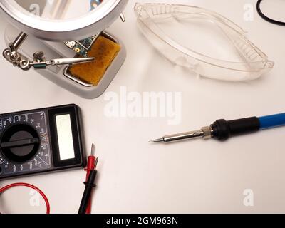 Immagine degli strumenti di riparazione elettronici, costituiti da un supporto per circuito stampato, saldatore, multimetro e occhiali protettivi. Spara su un dorso bianco isolato Foto Stock