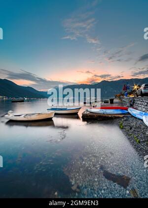 Il sole di fine estate tramonta dietro le montagne lontane e le barche sulla Baia di Cattaro. Foto Stock