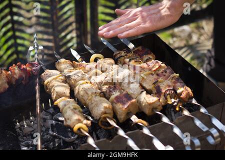 La carne pronta sgranò il kebab sugli spiedini in un braciere. La mano controlla il calore Foto Stock
