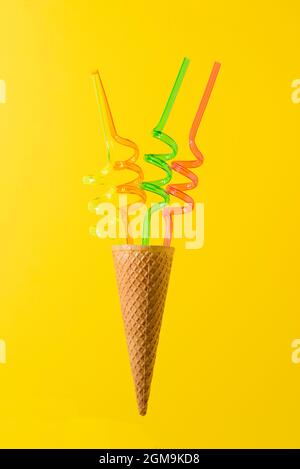 Concetto estivo minimale composto da coni per gelato e tubi per succhi colorati. Isolato su sfondo giallo. Foto Stock