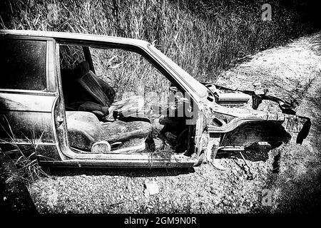 Carcassa di un'auto senza porte e copertura del cofano abbandonata in natura in stile bianco e nero Foto Stock