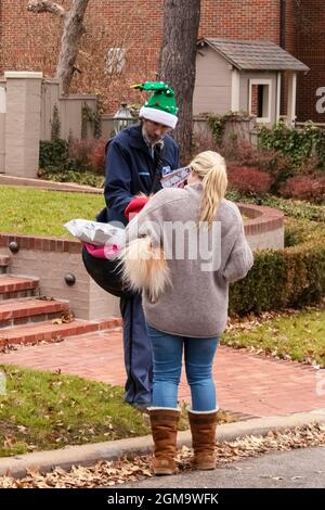 12-7-2018 Tulsa Stati Uniti d'America - Postman che indossa elfo verde cappello di Natale pausa nei suoi giri per il cane da compagnia tenuto da bella bionda donna di quartiere in maglione e. Foto Stock