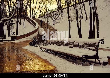 Panchine innevate nel parco, tramonto dorato Foto Stock