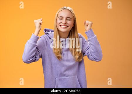 Trionfante festeggiamento positivo leale-capelli giovane femmina vincitore alzare mani clench pugni in su vittoria successo gesto chiudere occhi sorridendo ampiamente gla Foto Stock