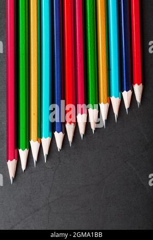 Matite di colori diversi in una fila su uno sfondo nero testurizzato. Vista dall'alto Foto Stock