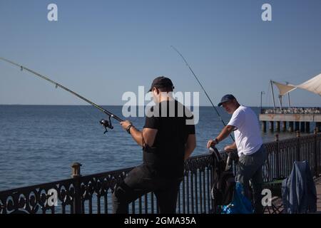 due uomini che hanno una conversazione mentre pescano su un molo. esprimendosi a vicenda. vita familiare Foto Stock