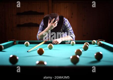 Un uomo con una barba svolge un grande biliardo. Partito in 12-piede piscina. Biliardo nel club gioco per gli uomini. Un uomo con un cue si rompe la piramide. Foto Stock