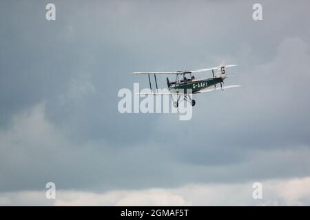 G-AAHI - a 1929 De Havilland DH-60G Gipsy Moth che vola basso e lento sotto il cielo nuvoloso Foto Stock