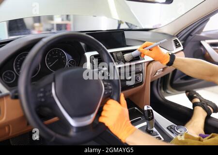 Pulizia manuale dell'interno dell'auto con spazzola per punti difficili da raggiungere in primo piano sul cruscotto Foto Stock