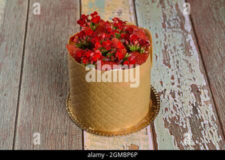 Primo piano di un dolce vestito, avvolto in uno strato testurizzato di caramello al cioccolato salato, con fragole e fiori rossi di kalanchoe. Foto Stock