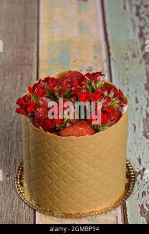 Vesti la torta, avvolta in uno strato testurizzato di cioccolato al caramello salato, con fragole e fiori rossi di kalanchoe (foto verticale). Foto Stock