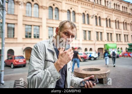 L'uomo europeo fuma sigarette elettroniche su strade affollate. Foto Stock