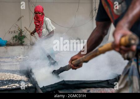 Dhaka, Bangladesh. 17 settembre 2021. DHAKA, BANGLADESH - 17 SETTEMBRE 2021: Un lavoro stradale migrante fonde i minerali di asfalto su piccole pietre per fare una miscela come parte del ripavimentamento di una strada in uno dei sobborghi di Dhaka, i dipendenti lavorano duramente diverse ore al sole per mantenere le strade e le strade della città in buone condizioni. Il 17 settembre 2021 a Dhaka, Bangladesh. (Foto di Tanvir Ahammed/ Eyepix Group) Credit: Eyepix Group/Alamy Live News Foto Stock