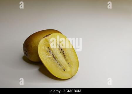 Primo piano di un Kiwifruit d'oro o di una bacca cinese (Actinidia chinensis) tagliata longitudinalmente e di una bacca intera su sfondo bianco Foto Stock