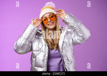 Elegante sassy audace bionda europea ragazza che agisce fresco indossare elegante occhiali da sole giacca argento cappello invernale controllo cornici naso testa inclinabile sorridente allegro Foto Stock