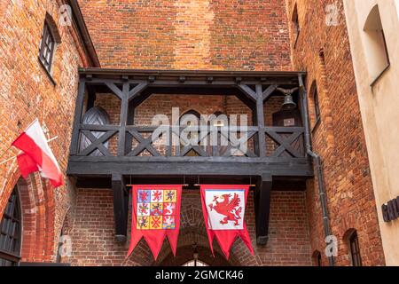 Vista sulle mura del castello gotico di Darłowo. Mattoni rossi e tegole rosse compongono l'architettura del castello. Bandiere e balcone in legno Foto Stock