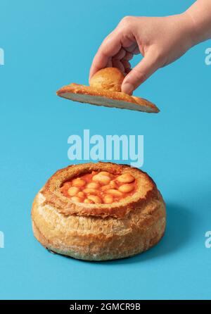 Fagioli cotti in una ciotola fatta da una pagnotta di pane. Piatto tradizionale con fagioli bolliti con salsa di pomodoro in crosta di pane. Foto Stock