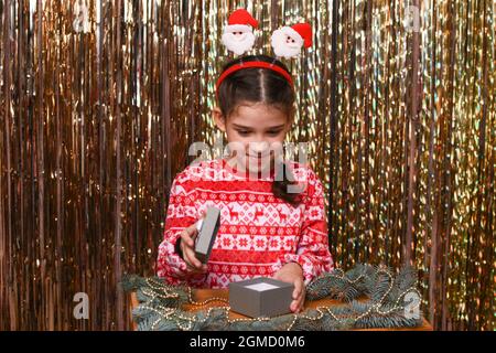 una ragazza apre una scatola del regalo su uno sfondo dorato. Foto Stock