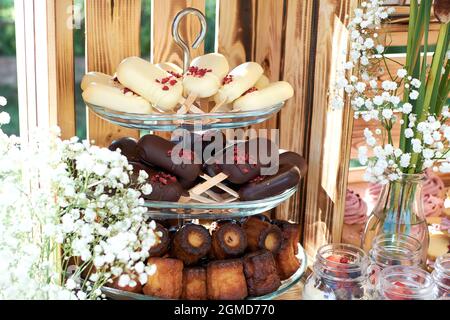 Frammento di un tavolo da dessert. La torta schiocca in difficoltà e cioccolato fondente e cannellé. Gypsophilia in forma di decorazione, sfondo in legno Foto Stock