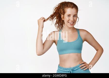 Bella donna rossa sorridente alla macchina fotografica. Fitness ragazza che indossa sportsbra per l'allenamento, preparati per gli esercizi, sfondo bianco Foto Stock