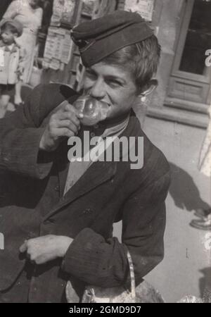 vintage photograp degli anni '40 o '50 un ragazzo era stato shopping ma aveva fame che non poteva aspettare di tornare a casa, quindi stava mangiando un piccolo pane di sfida. Poi aveva sparato così è per questo che sta sorridendo a noi proprio ora. Foto Stock