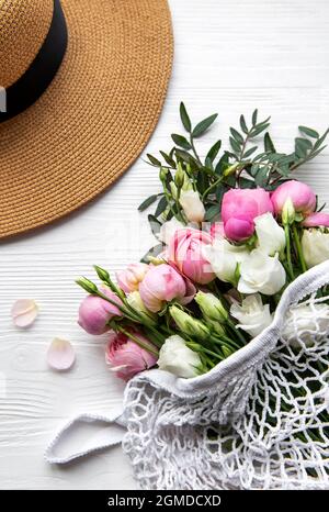 Cappello di paglia e bouquet di fiori rosa rosa su sfondo bianco. Vista dall'alto, composizione minima in stile di posa piatta. Concetto di vacanza estiva. Foto Stock