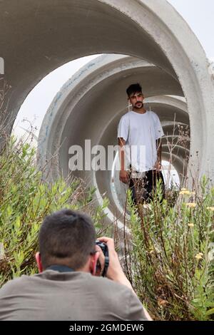 Fotografo che scatta foto di un giovane modello di brunetta bianca con barba e baffi all'interno di un grande tubo di cemento Foto Stock