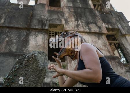 Donna che indossa maschera testa dinosauro contro l'orrore rovinato casa abbandonata Foto Stock