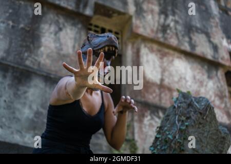 Donna in maschera di dinosauro gesturing con Hands.Halloween paura terrore concetto Foto Stock