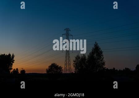 Vista di un traliccio incrociato e linee elettriche ad alta tensione al tramonto con la silhouette dell'albero di fronte e spazio copia Foto Stock